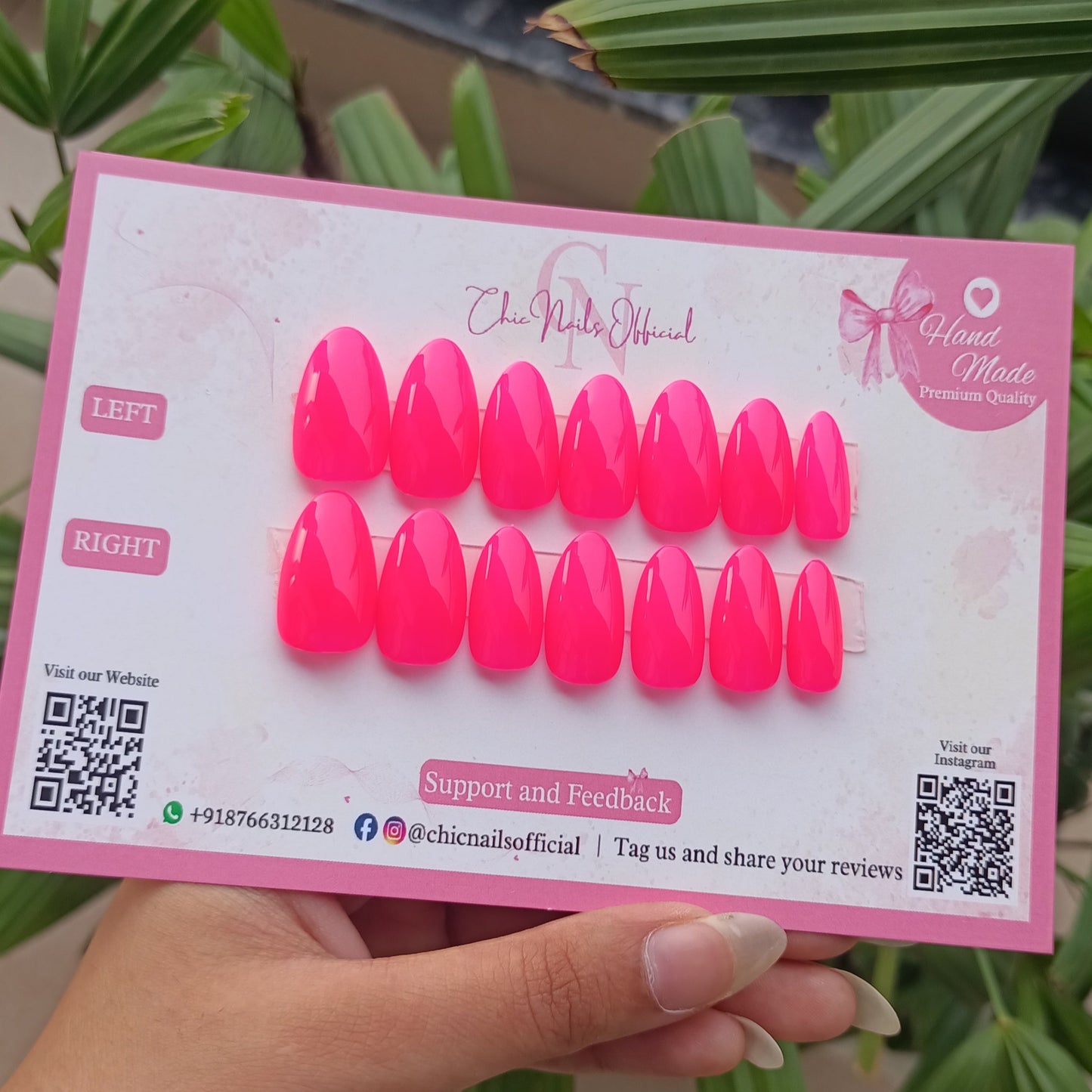 holding a pack of neon hot pink false nails with a green plant in the background