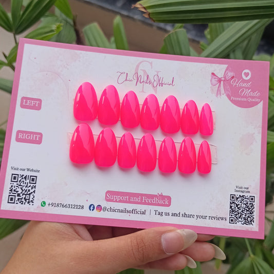 holding a pack of neon hot pink false nails with a green plant in the background